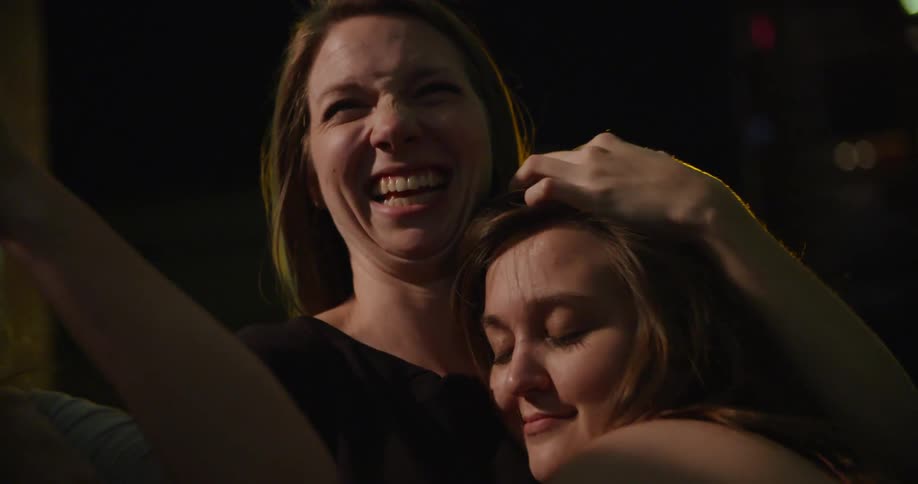 Three women laugh and talk and one leans over and hugs another