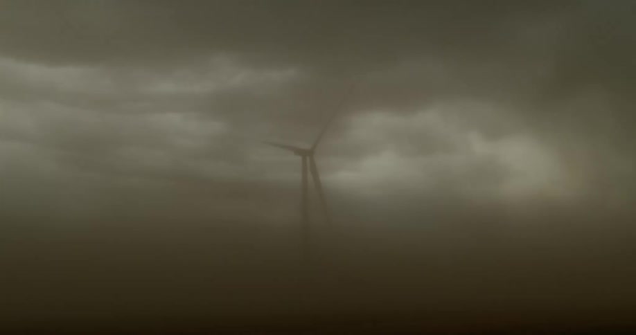 Mist and clouds floating in front of a rotating wind turbine