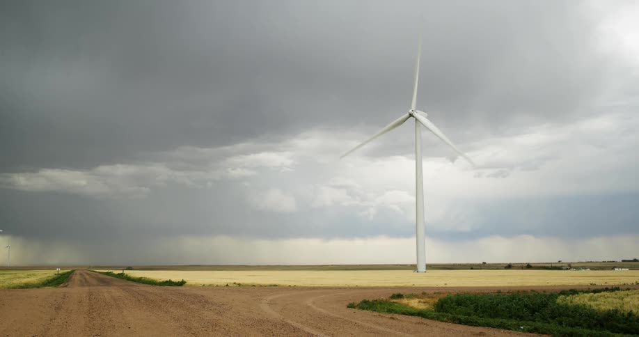 Storm clouds float above a rotating wind turbine in a rural field