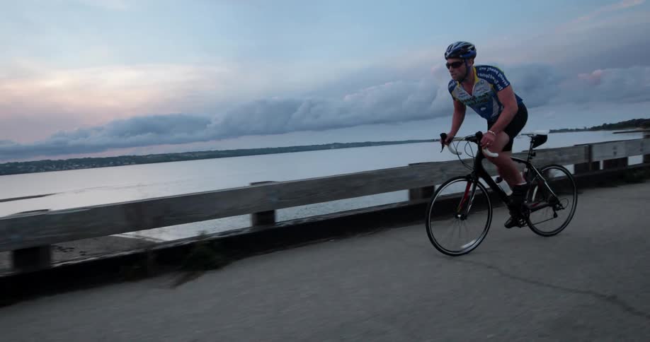 A man with a helmet and sunglasses riding a bike near the coast