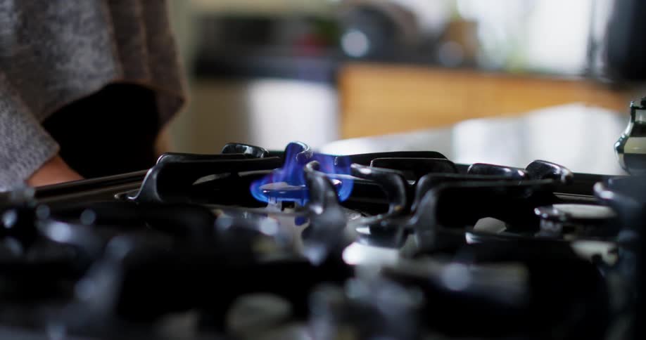 A woman turns on a gas burner on a stove at home