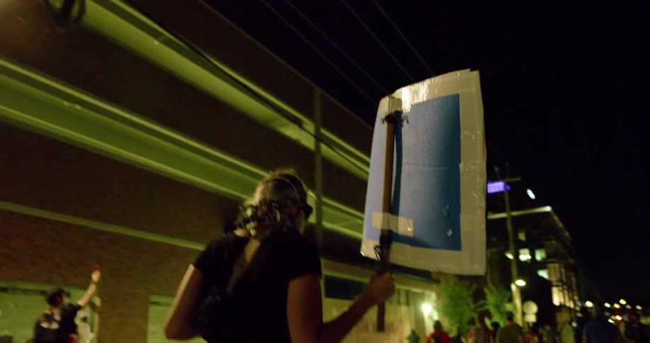 People carrying signs march down a city street and protest while a police officer stands by