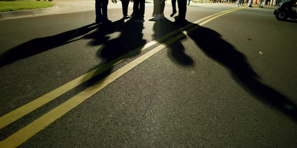 People stand and walk along asphalt road as their shadows cross double yellow line