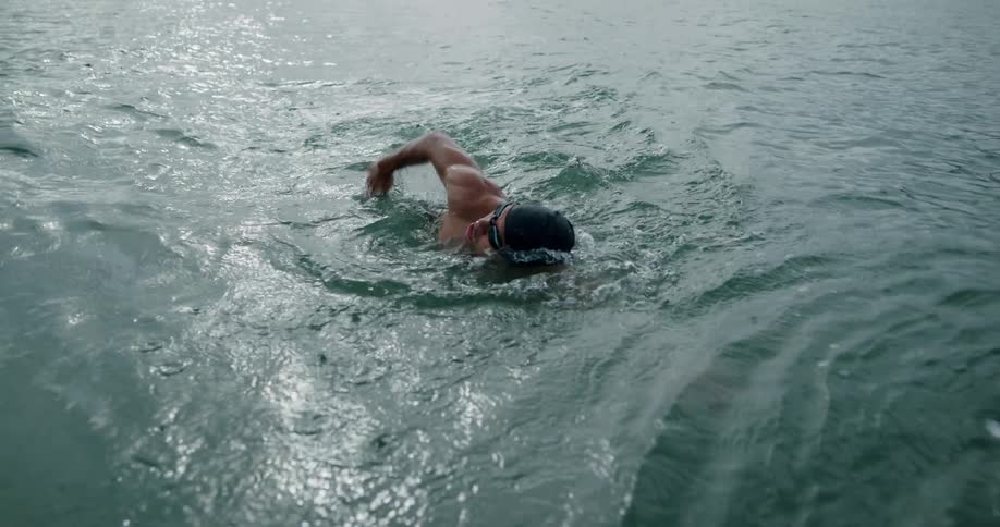 Muscular man with goggles anda swim cap swims through sea water