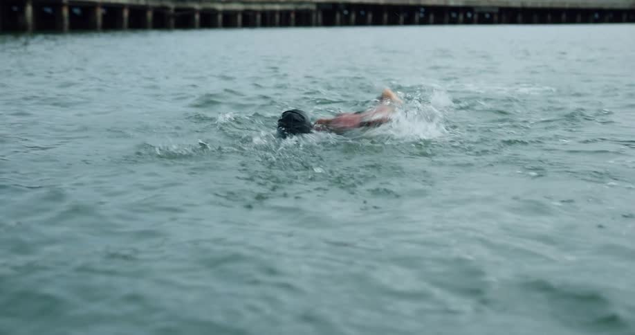 A man is swimming in the water by the pier