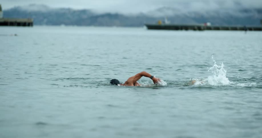 A male swimming in a river near boats