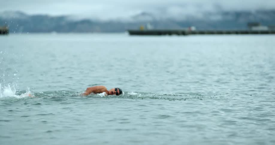 A swimmer dunks his head under the lake water and then starts to swim