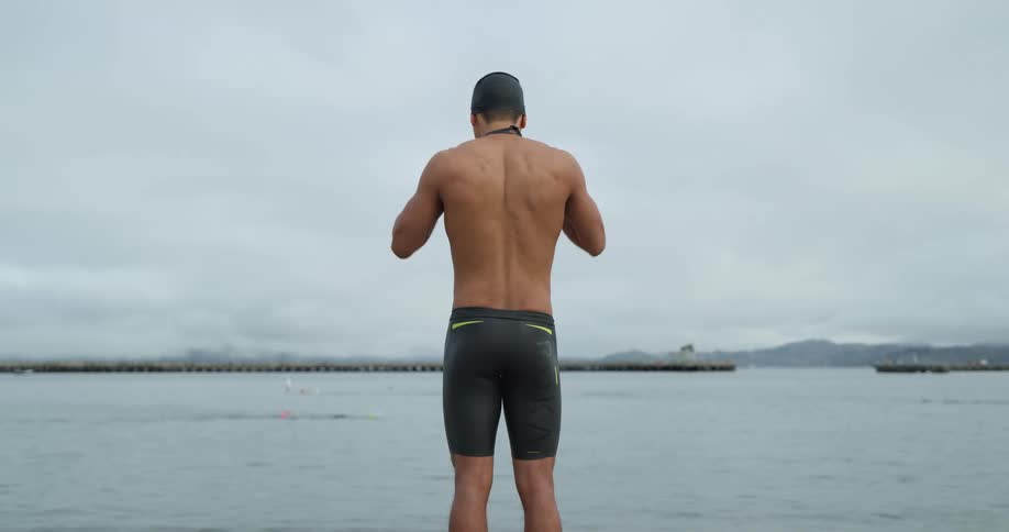 A man adjusts swimming cap and goggles as he prepares to swim in a bay on a cloudy day