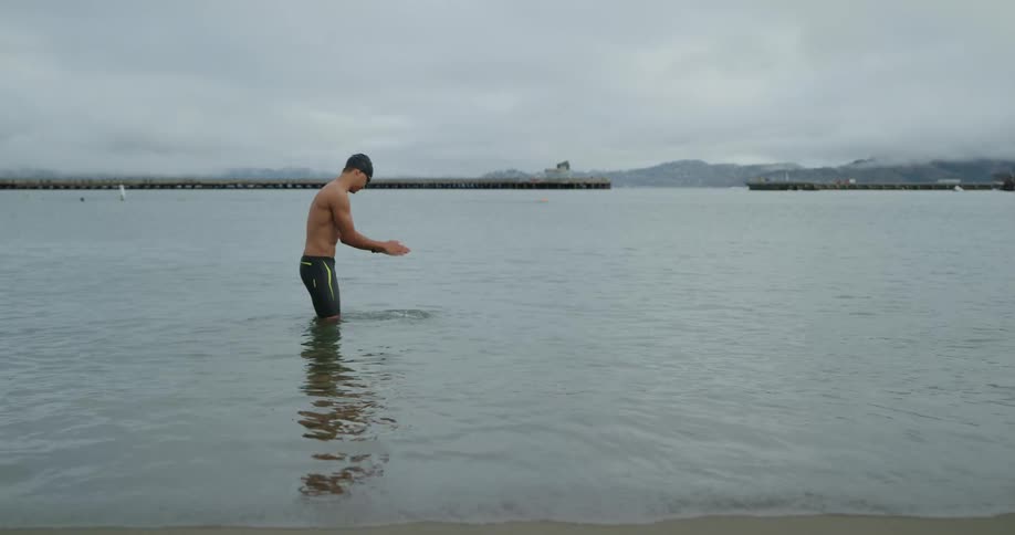 A young man splashes water on his arms before starting an open water swim