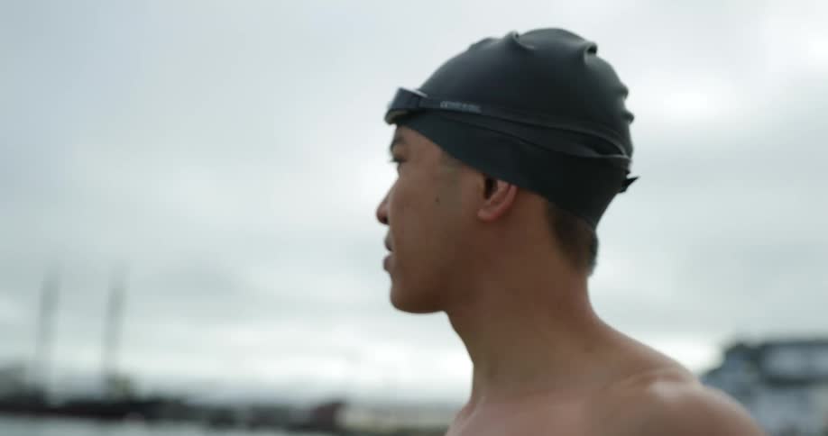 A swimmer standing on the shore stretches and warms up his muscles before getting in the water