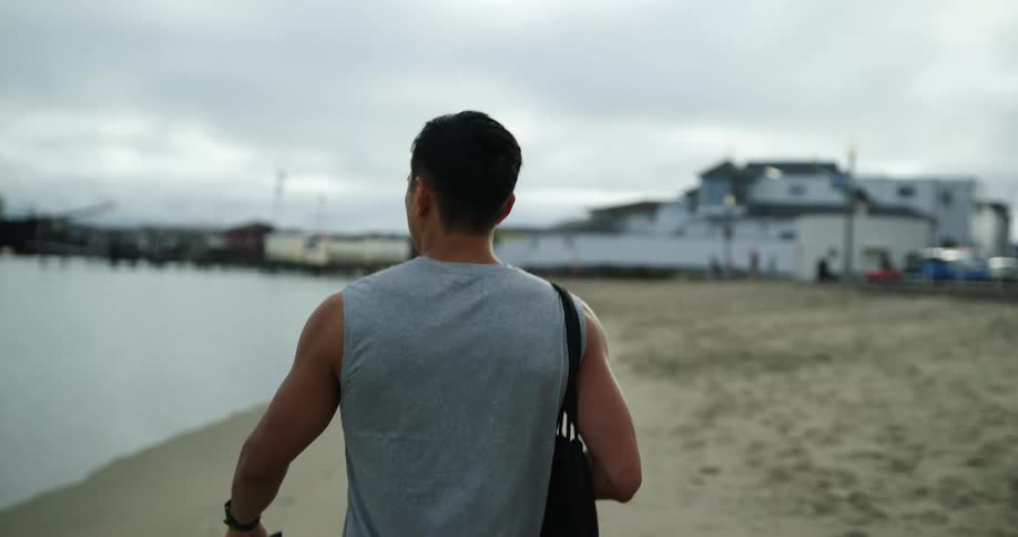 Man walks across beach toward buildings carrying bag