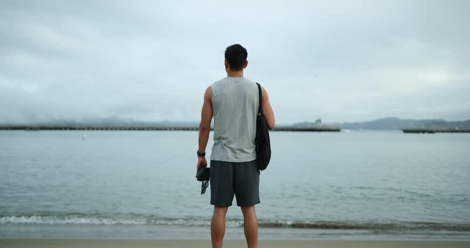 A man stands on the beach looking to the water