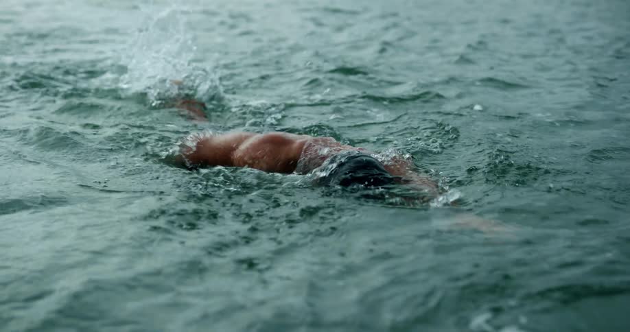 Muscular man with goggles anda swim cap swims through water