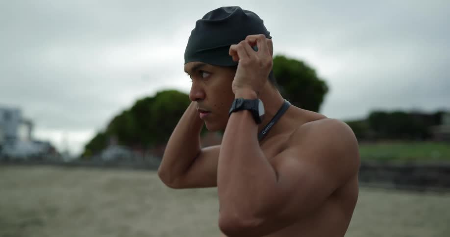 A young man on the beach puts his swim cap on as people walk behind him