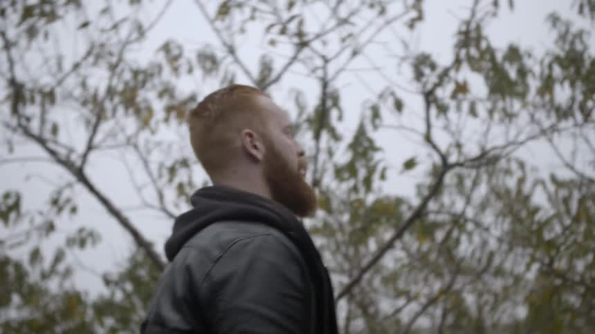 A bearded man walks among trees