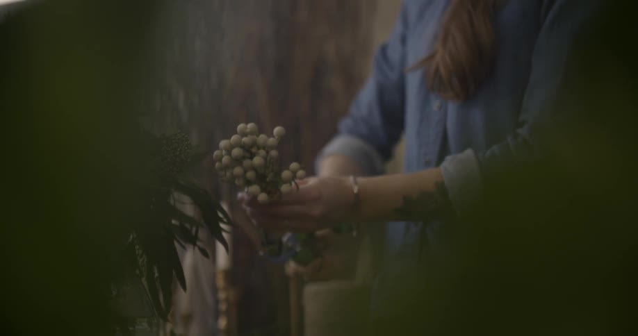 A woman cuts bunches of wildflowers while standing outside at a table