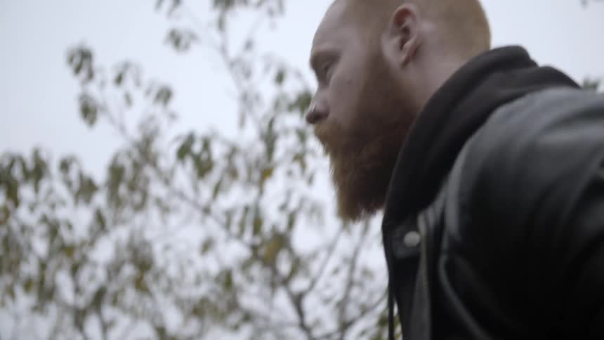A bearded man walks next to some trees