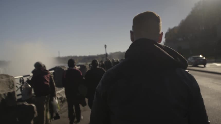 A man is walking down a road by a waterfall with many people standing around