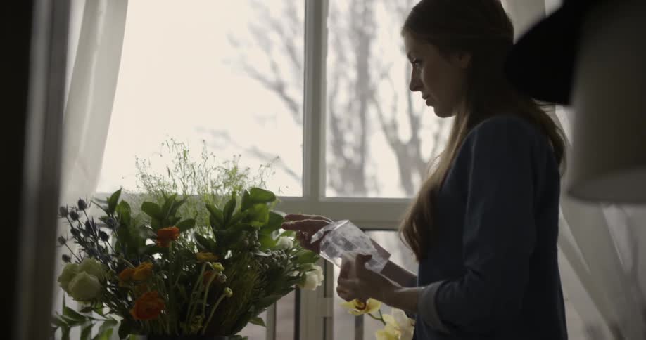 A woman is arranging flowers by a window
