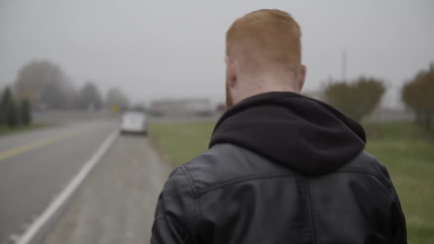 A red headed man walks down the side of a road