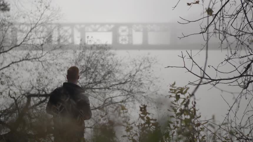 A man in a jacket stands near a tree