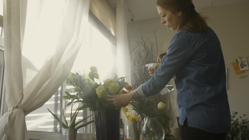 A woman sprays water onto a flower arrangement