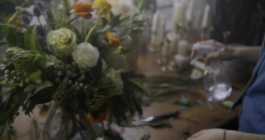 A woman straightening a flower arrangement and misting it with water