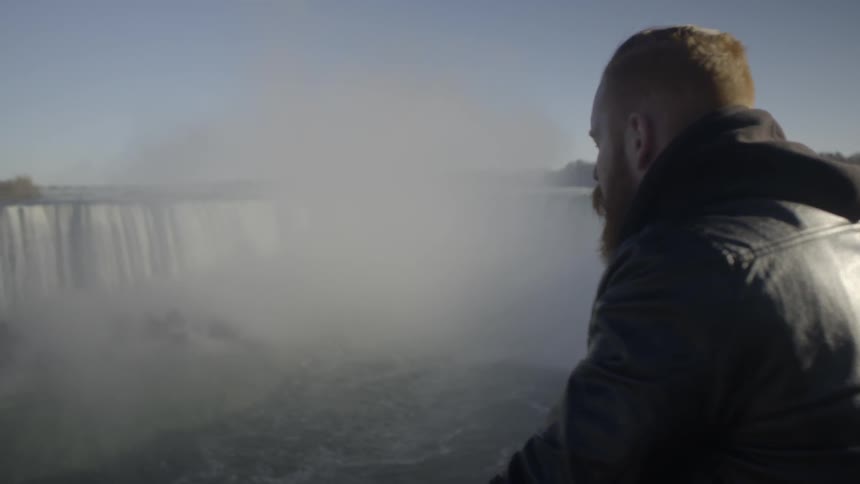 A man stands looking out at a very large waterfall