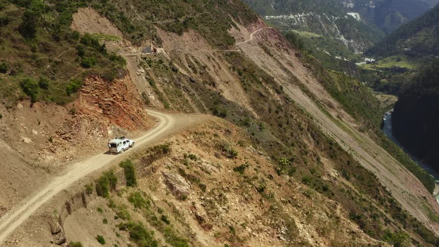 A car is driving in a rural area next to the mountain