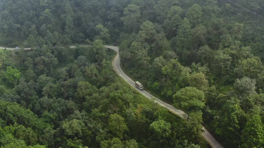 An aerial view of a truck traveling on a winding forest road in the daytime