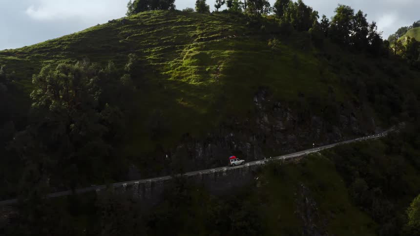 An aerial view of a car traveling on a mountain road on a summer day