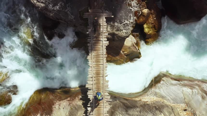 A group of hikers cross a narrow wooden bridge over a ravine
