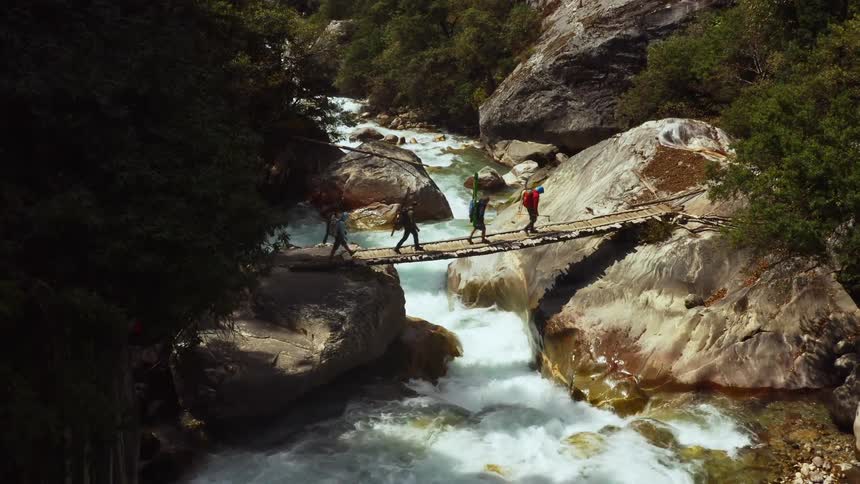 Four peole walk across a small pedestrian bridge thats overtop of a running river
