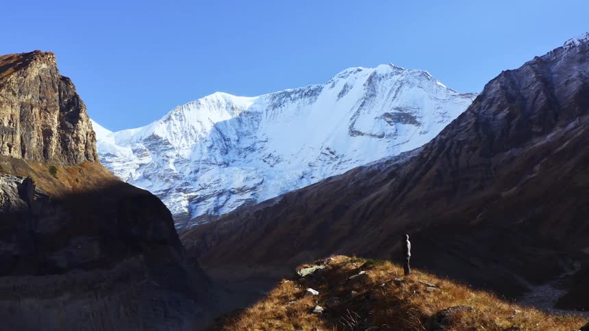 A person standing on a hill with a snow covered mountain range in the background