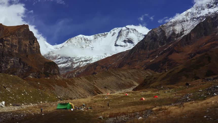 Four people walking around tents at the base of a mountain