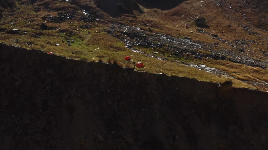 One side of ridge is a cliff and the other contains a camp with people walking around