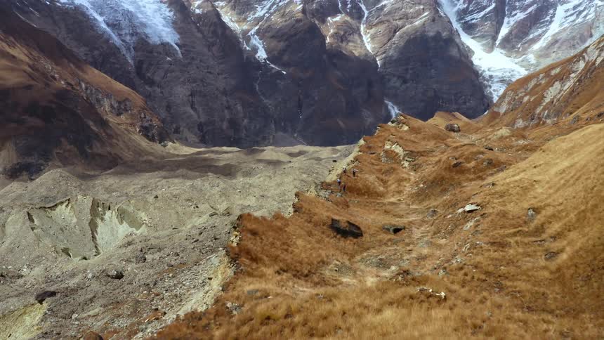 A group of hikers walk along a mountain ridge in single file during the day
