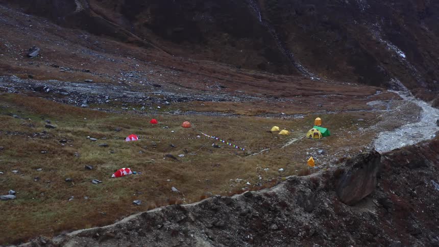 Campsite with multiple tents on plateau in tall mountain range