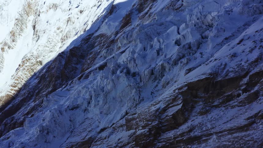 A jagged snow covered mountain slope cloaked in the shadow of a nearby peak