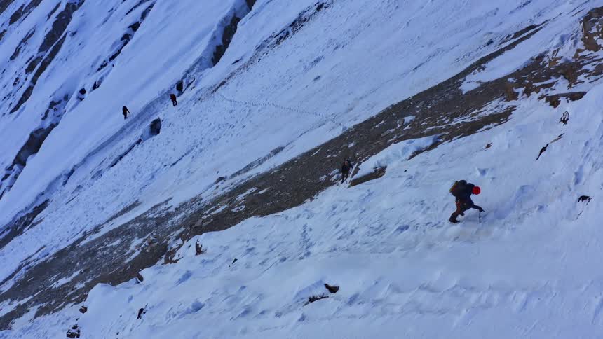A group of hikers climb a steep snowy mountain slope in the evening