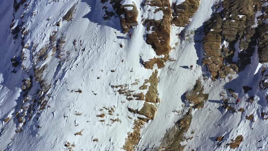 A group of hikers climb a snowy mountain ridge at high altitude on a sunny day