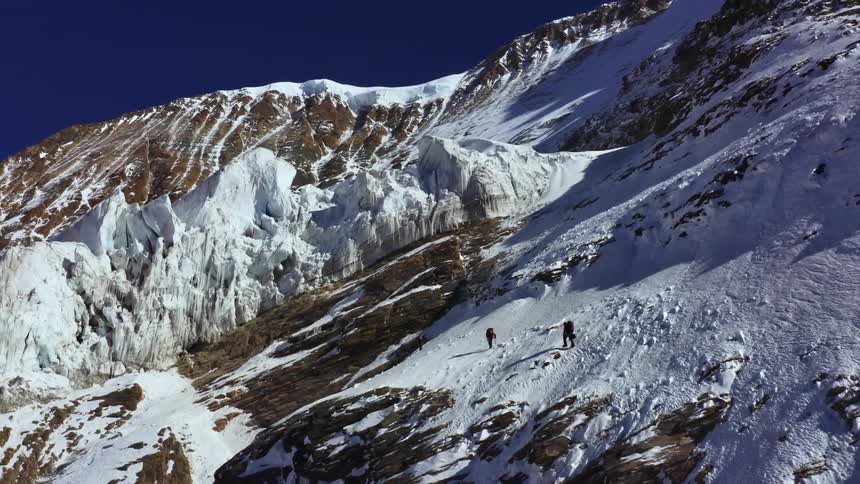 Two people hike along the slope of a snow covered mountain