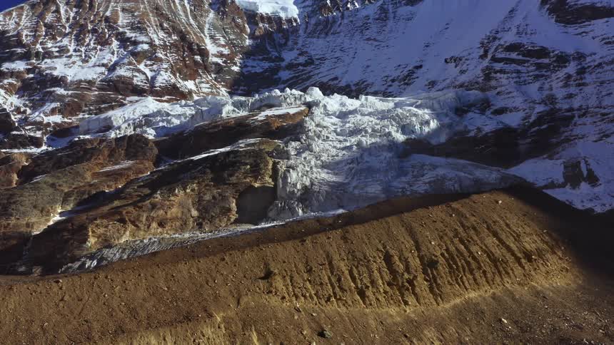 A mountain ridge with one half covered in compacted snow and the other bare soil
