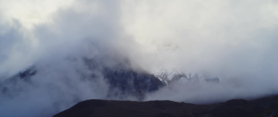 Clouds of fog shroud a snowy mountain summit during the day