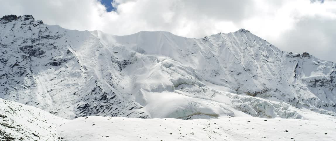 Clouds pass over a snow covered mountain ridge on a bright day