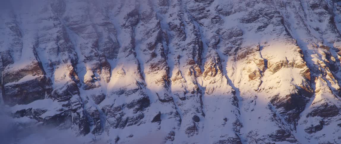 A rocky mountain slope covered in snow in the evening