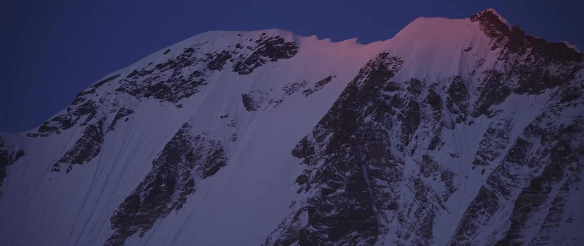 An orange light shining on the summit of a snowy mountain slowly fades