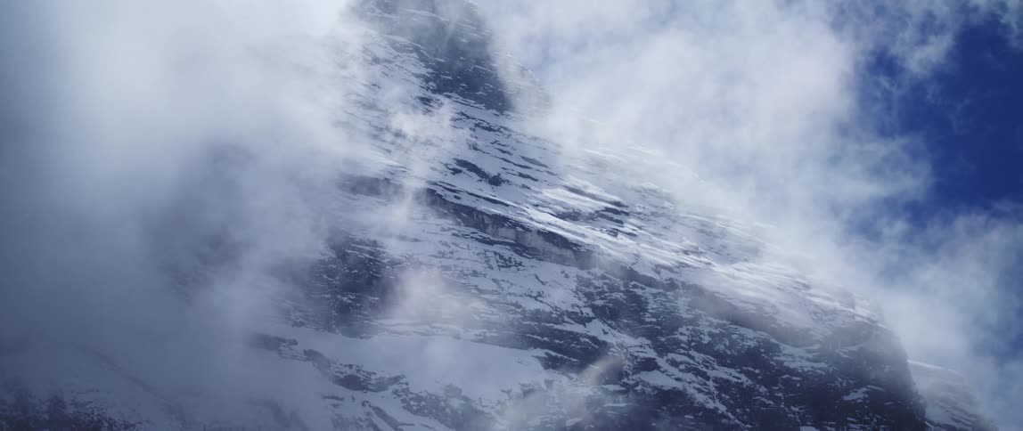 A mountain range with snow and ice with the sky and clouds above