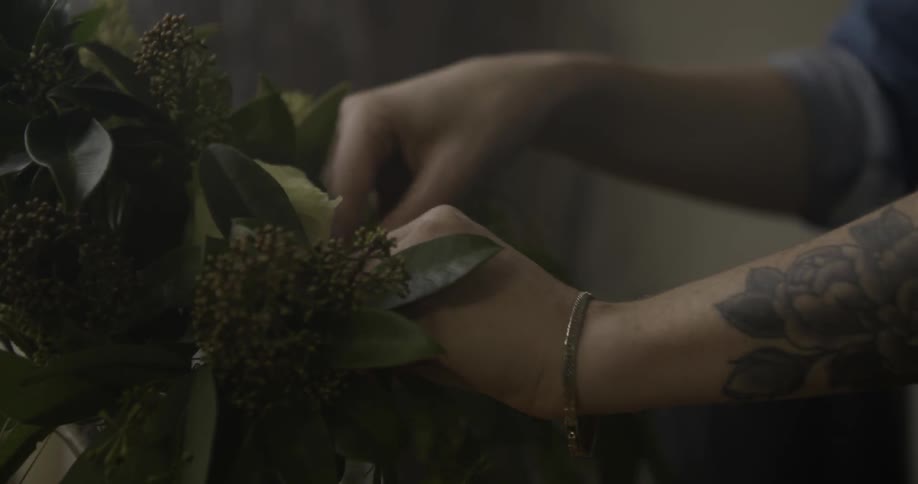 A woman's hands are seen arranging foliage and flowers in a vase