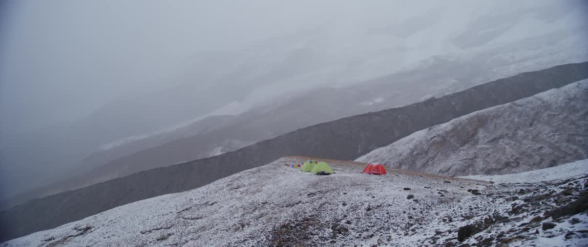 Three tents on a land covered with snow with a mountain range the sky and clouds in the background